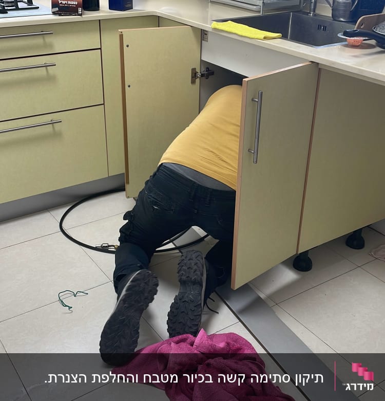 אדם מתקן צנרת מתחת לכיור במטבח